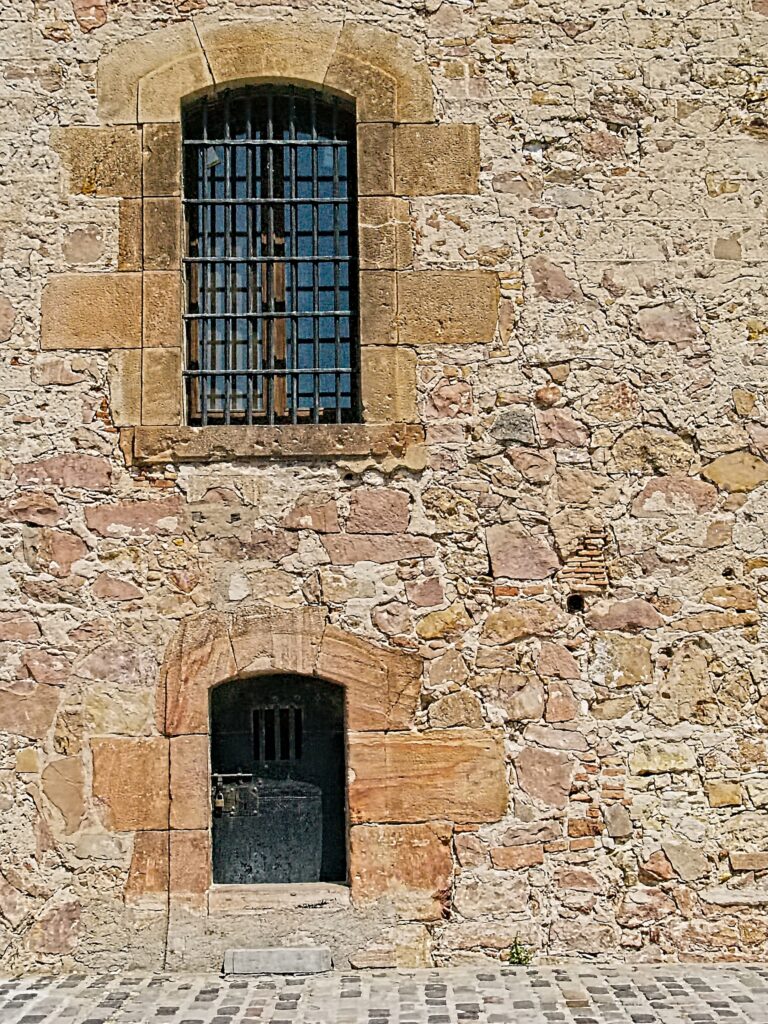 The image captures a rustic stone wall featuring a wooden door and a barred window. The irregular texture of the stone gives the structure an aged appearance.